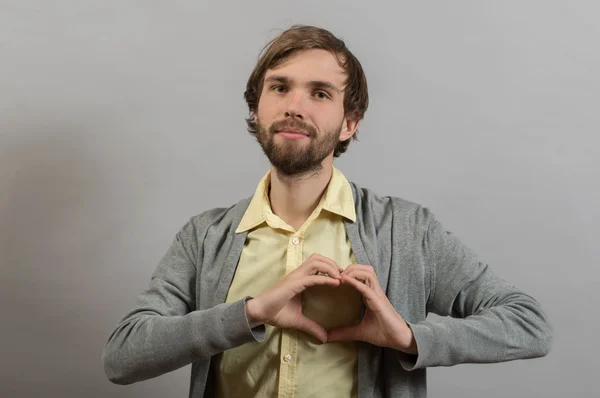 Retrato de jovem fazendo gesto de coração contra um fundo cinza — Fotografia de Stock