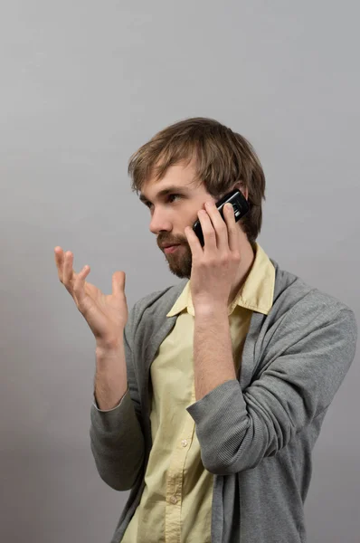 Um homem a falar ao telefone. Em um fundo cinza . — Fotografia de Stock