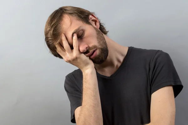 Alın ağrı gri arka plan üzerinde tutan genç yorgun adam portresi