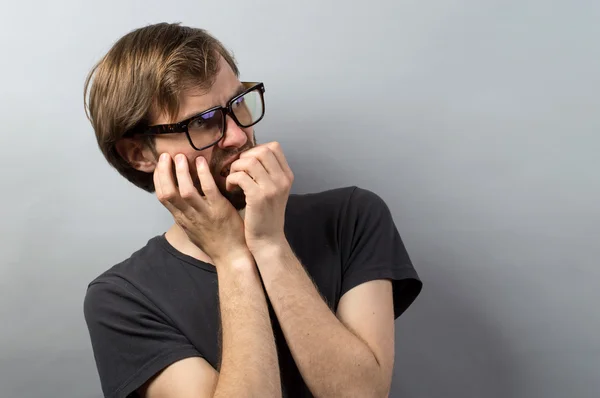 Young man biting his nails on a light gray studio background — Stock Photo, Image