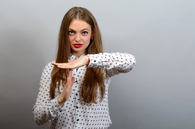 Young woman with a little smile showing time out hand gesture, isolated on grey wall background. clipart