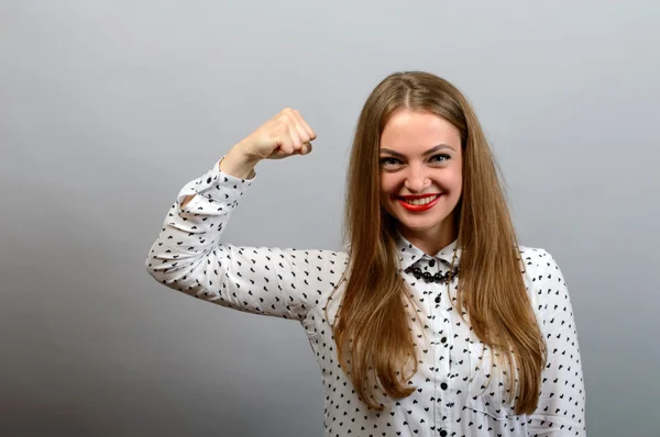 Mujer joven señala a las manos fuertes. Sobre un fondo gris . —  Fotos de Stock