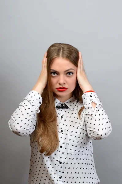 Porträt einer jungen Frau, die ihre Ohren vor grauem Hintergrund verhüllt. Blick in die Kamera — Stockfoto