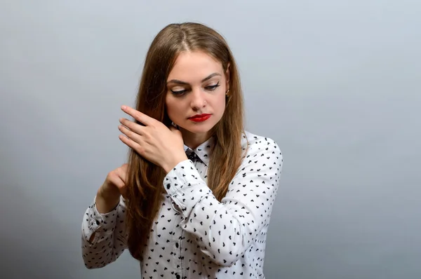 La mujer endereza su cabello. Sobre un fondo gris . — Foto de Stock