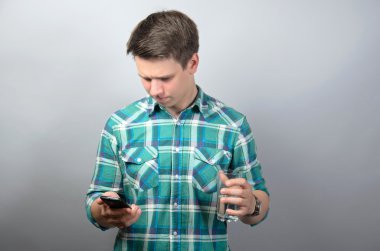 Smartphone kullanarak ve gri arka plan üzerinde bardak su tutan adam