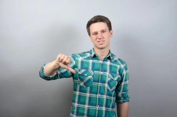 Joven mostrando pulgares hacia abajo sobre un fondo gris — Foto de Stock