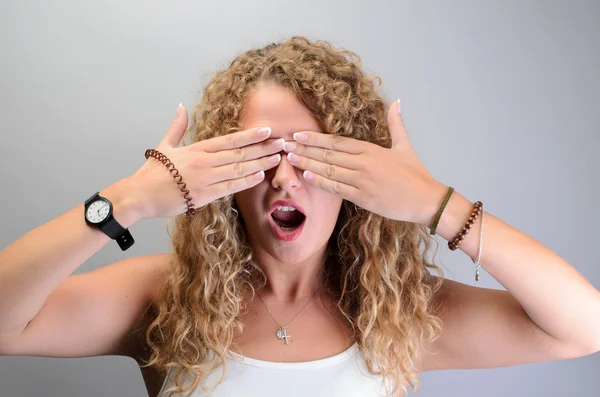 Junges lockiges Mädchen, das ihre Augen mit geöffnetem Mund bedeckt — Stockfoto