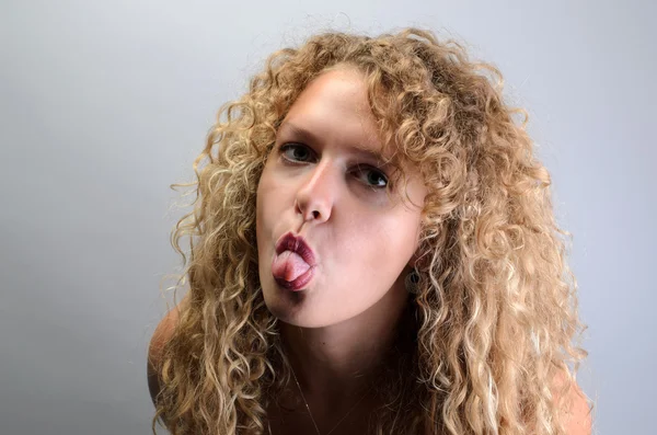 La chica rizada muestra la lengua. Fondo gris . —  Fotos de Stock