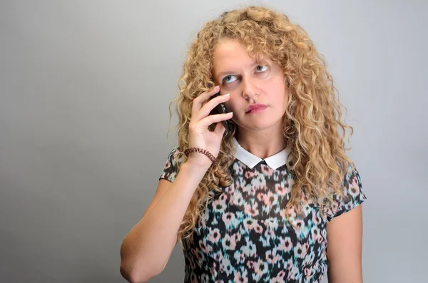Кудрявая женщина разговаривает по телефону на сером фоне — стоковое фото
