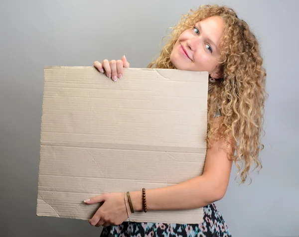 Menina feliz segurando placa em branco sorrindo no fundo cinza — Fotografia de Stock