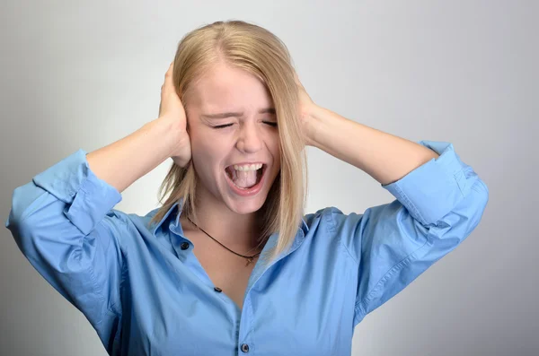 Portrait of a young woman closing her ears and screaming on gray background — Stock Photo, Image