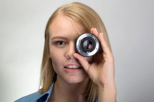 Mujer joven usando lente de cámara sobre fondo gris — Foto de Stock