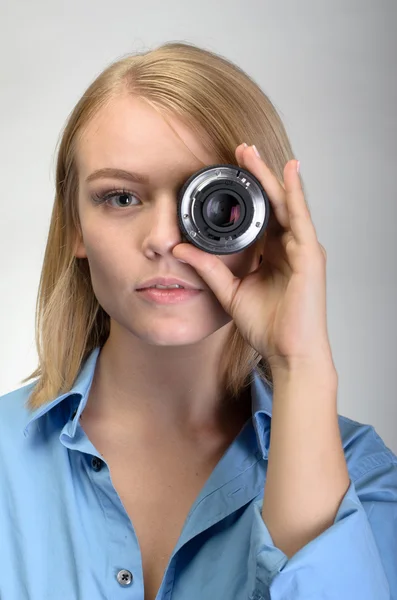 Mujer joven usando lente de cámara sobre fondo gris — Foto de Stock