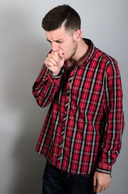 Yumruğuna öksüren bir adam. Gri arkaplan