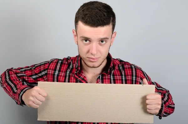 Portrait of young man showing blank signboard, with copyspace area for text or slogan, against grey background — Stock Photo, Image