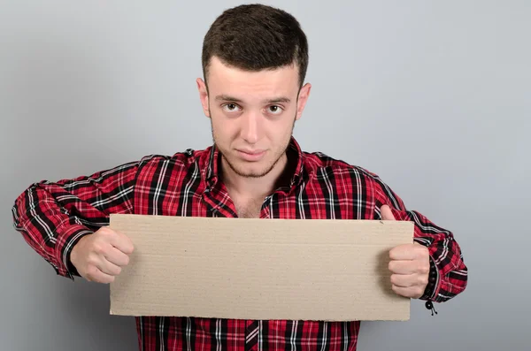 Portrait of young man showing blank signboard, with copyspace area for text or slogan, against grey background — Stock Photo, Image