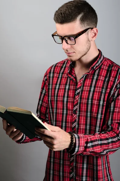 Joven estudiante con gafas y libro de lectura sobre fondo gris — Foto de Stock