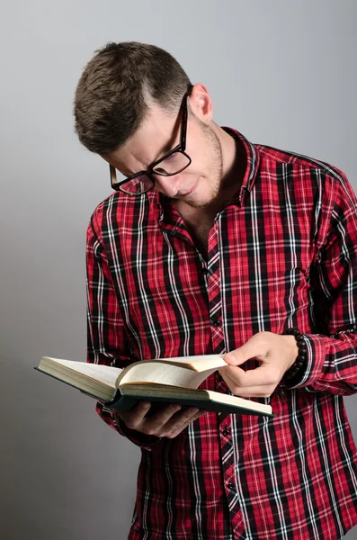 Young student wearing glasses and reading book on grey background — Stock Photo, Image