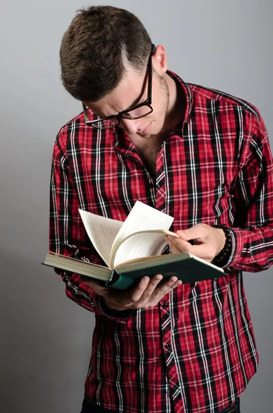 Young student wearing glasses and reading book on grey background — Stock Photo, Image