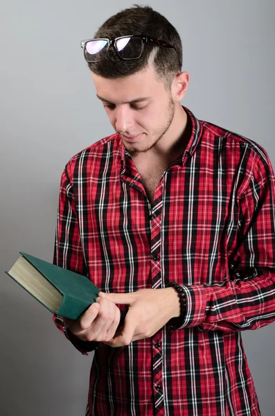 Young student wearing glasses and reading book on grey background — Stock Photo, Image