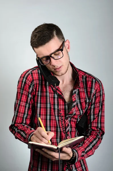 Joven hablando por teléfono fijo y escribiendo algo en la nota — Foto de Stock