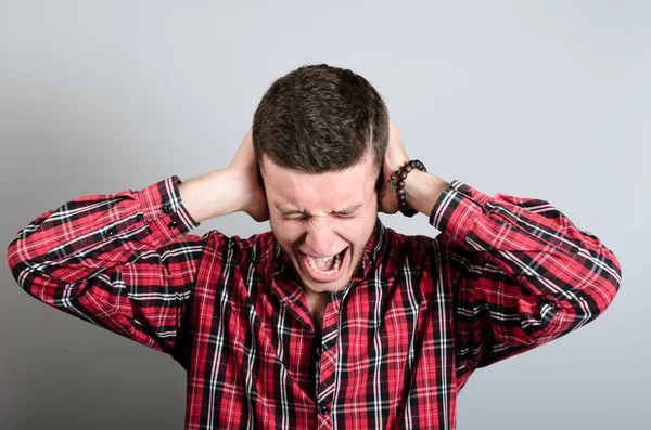 Grita y grita. Retrato de jóvenes furiosos sosteniendo la cabeza con las manos y gritando mientras están aislados en gris —  Fotos de Stock