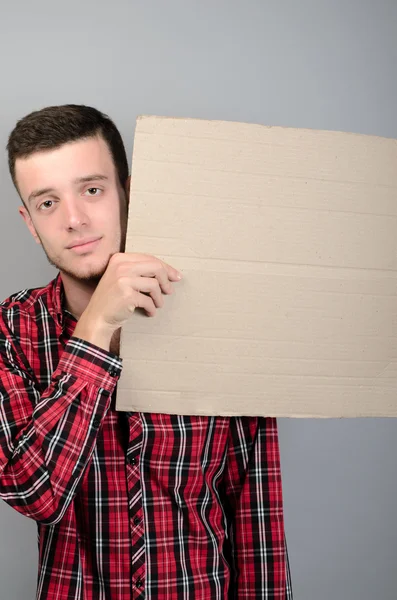 Retrato de un joven mostrando un letrero en blanco, con área de copyspace para texto o eslogan, sobre fondo gris — Foto de Stock