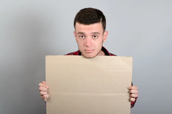 Retrato de un joven mostrando un letrero en blanco, con área de copyspace para texto o eslogan, sobre fondo gris — Foto de Stock