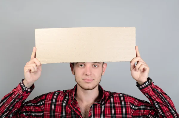 Portrait of young man showing blank signboard, with copyspace area for text or slogan, against grey background — Stock Photo, Image