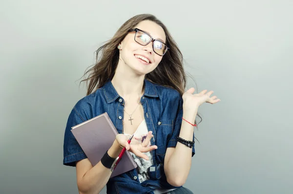 Jovem segurando caderno com uma caneta em fundo cinza — Fotografia de Stock