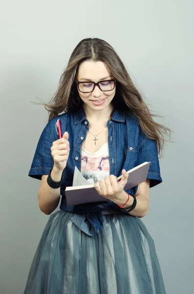 Jovem segurando caderno com uma caneta em fundo cinza — Fotografia de Stock