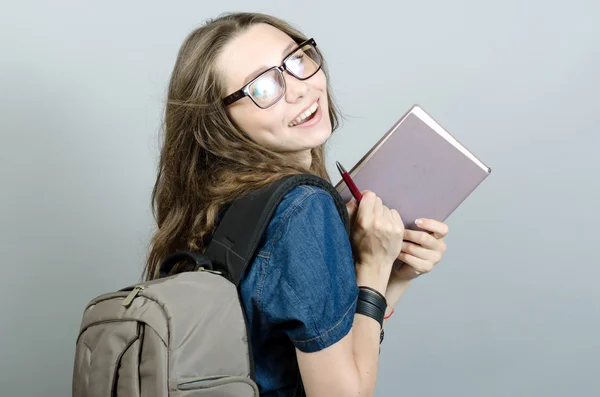 Jovem segurando livro com mochila em fundo cinza — Fotografia de Stock