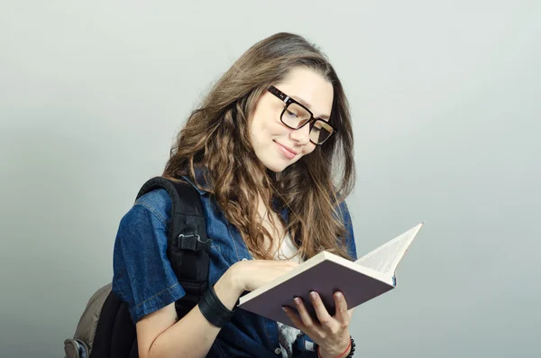 Young woman holding book with backpack on grey background — Stock Photo, Image