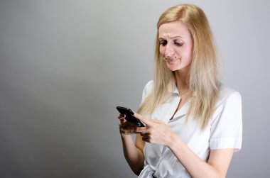 Genç kızgın kadın mutsuz, rahatsız bir şey, onun cep telefonu SMS kötü sms metin mesajı haber alma, birinde gri duvar arka plan izole