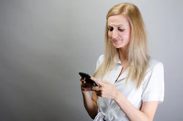 Молода сердита жінка незадоволена, чимось дратує, хтось на її мобільному телефоні смс-повідомлення, отримує погане смс-повідомлення новини ізольовані сірі стіни фону — стокове фото