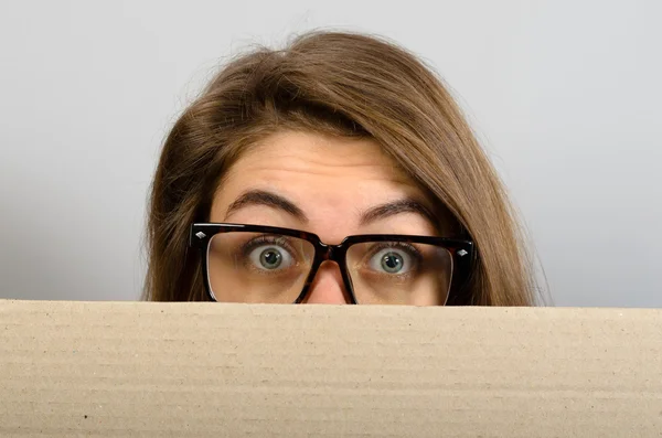 Banner segno donna sbirciando oltre bordo di cartellone vuoto vuoto. Bella giovane donna con gli occhiali guardando con gli occhi spalancati isolati su sfondo grigio — Foto Stock