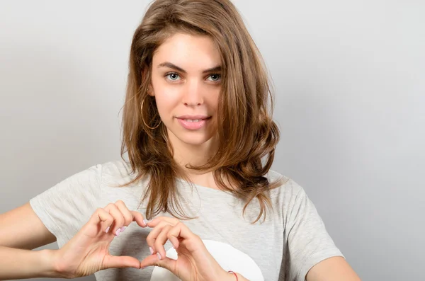 Hermosa mujer haciendo forma de corazón Señal contra fondo gris — Foto de Stock