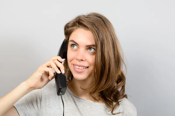 Šťastná mladá žena pomocí telefonu proti šedé pozadí — Stock fotografie