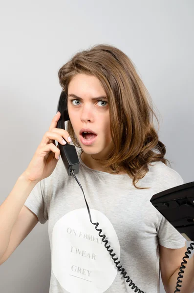 Menina chocada bonita com telefone antigo, no fundo cinza — Fotografia de Stock