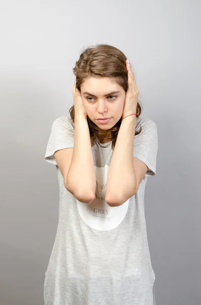Mujer joven con las orejas cerradas sobre fondo gris — Foto de Stock