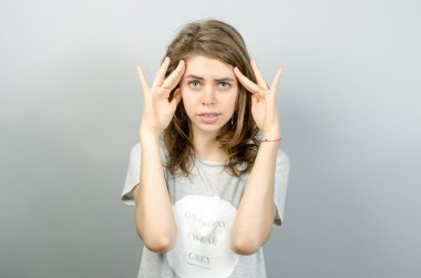 Sevimli kadın parmakları kafa yakınındaki düşünüyor. Gri arka planı.