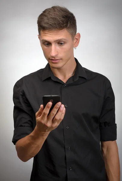 灰色の背景に対して立っている間携帯電話を保持している若い男をクローズ アップ — ストック写真