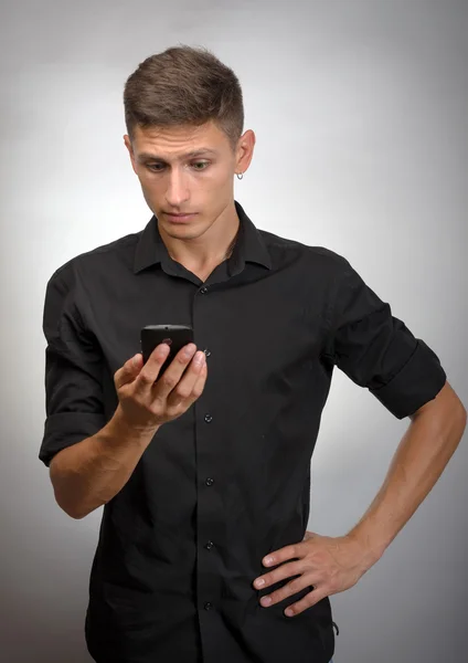 Primo piano del giovane che tiene il cellulare in piedi sullo sfondo grigio — Foto Stock