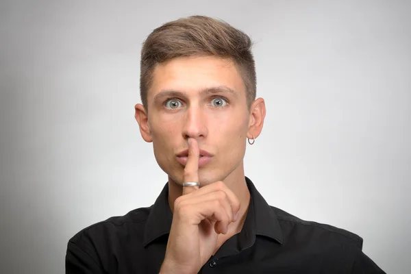 Homem pedindo para manter o dedo quieto perto da boca, isolado no fundo da parede cinza — Fotografia de Stock