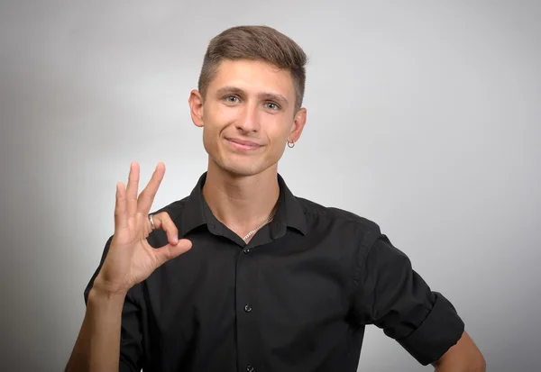 Retrato de un joven positivo sonriendo, guiñando un ojo y mostrando un signo aceptable — Foto de Stock