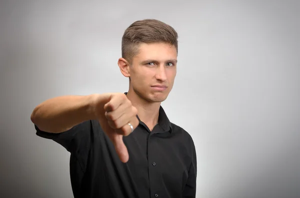 Fiatal férfi mutatja hüvelykujját le egy szürke háttér — Stock Fotó