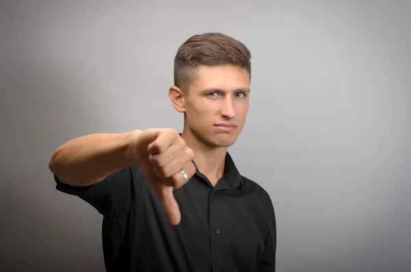 Joven mostrando pulgares hacia abajo sobre un fondo gris — Foto de Stock