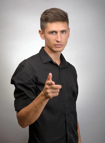 Joven con el dedo apuntando hacia la cámara sobre un fondo gris — Foto de Stock