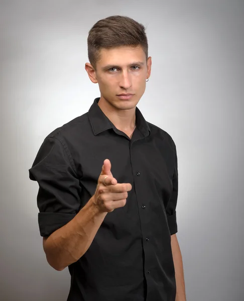 Joven con el dedo apuntando hacia la cámara sobre un fondo gris — Foto de Stock