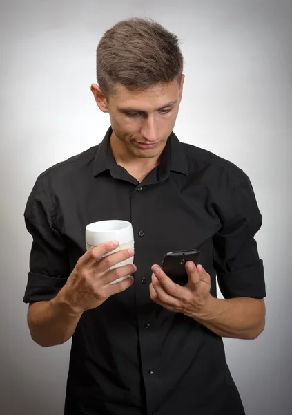 Portrét člověka dívá na mobil drží tea Cup — Stock fotografie